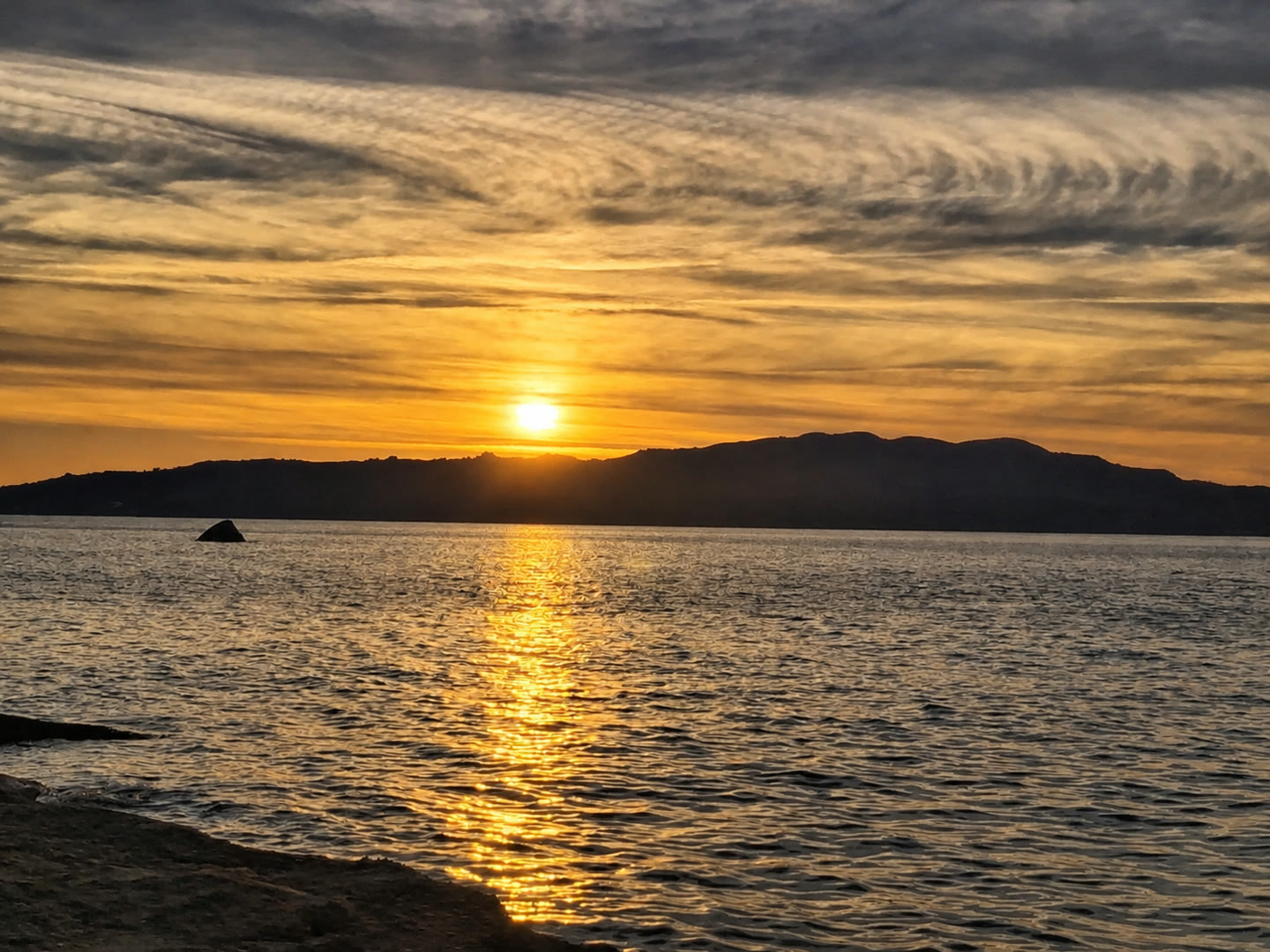 The sun setting over water behind a low island silhouette.